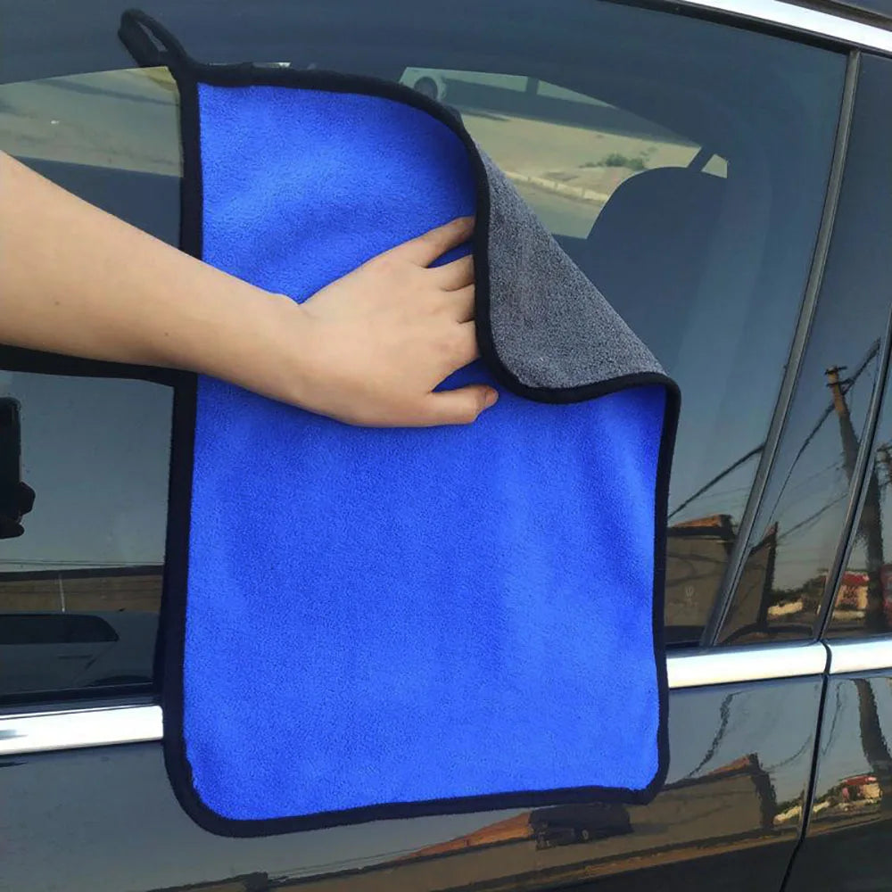 A hand is holding a bright blue microfiber car drying towel against the window of a vehicle.