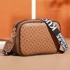 A brown patterned compact crossbody bag with black trim and a black strap resting on a light surface.