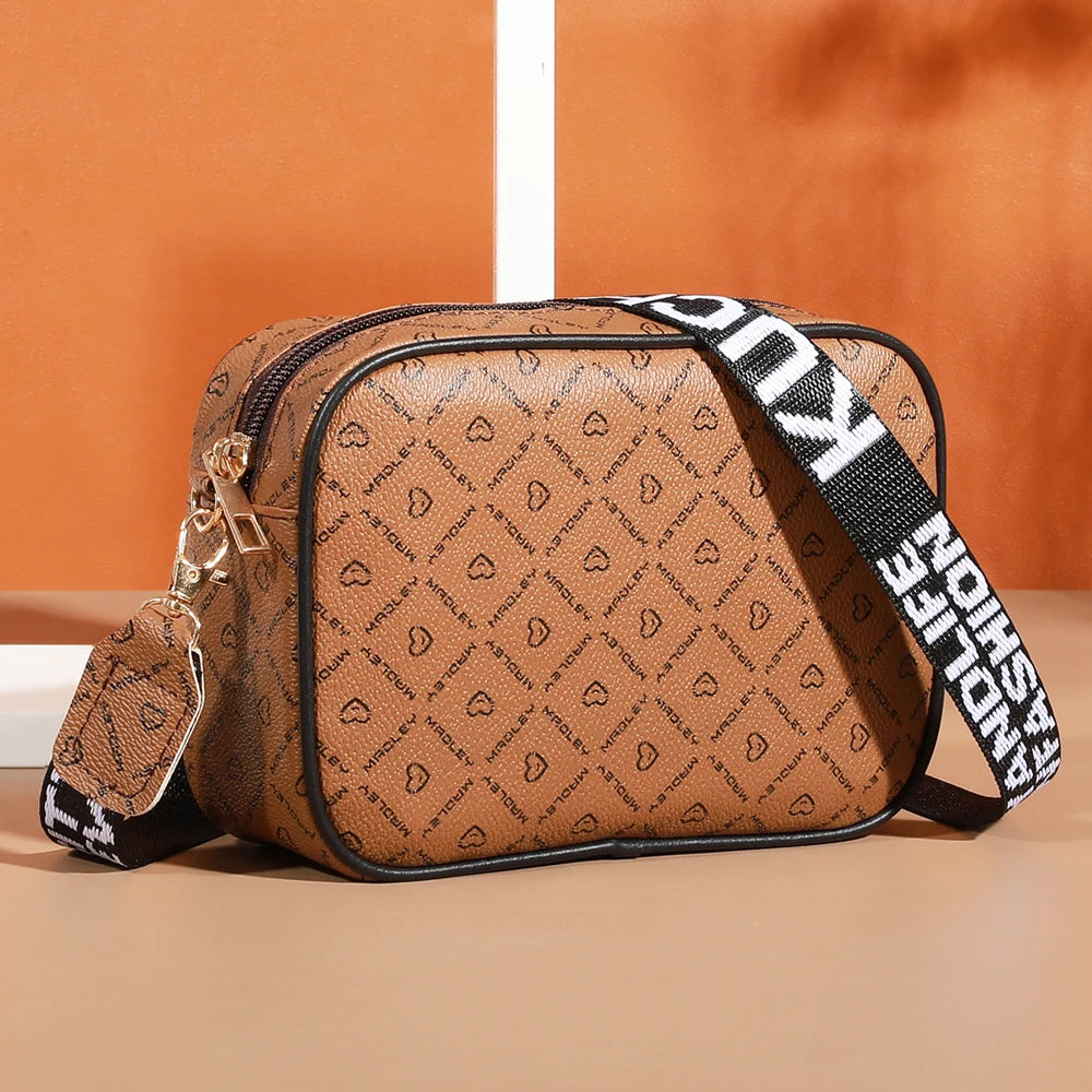 A brown patterned compact crossbody bag with black trim and a black strap resting on a light surface.