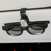 Black sunglasses with a rhinestone clip resting on a light-colored car visor.