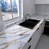 A kitchen countertop with a black sink set into a white marble effect surface featuring gold and blue veining.