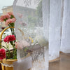 Un rideau blanc transparent avec broderie florale pend à côté d'un arrangement de fleurs roses et rouges en pot.