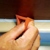 A hand is using an orange silicone tile grout filling tool to repair a home seam.