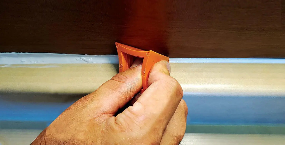 A hand is using an orange silicone tile grout filling tool to repair a home seam.