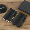 A black minimalist leather card holder with a bottle opener is shown on a wooden surface.
