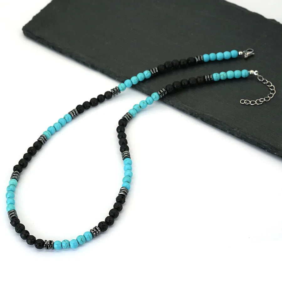 A beaded necklace featuring black and turquoise stones displayed on a dark slate background.