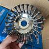 A hand holds a 6-inch steel wire wheel brush for string trimmers, showing the bristles and mounting plate.