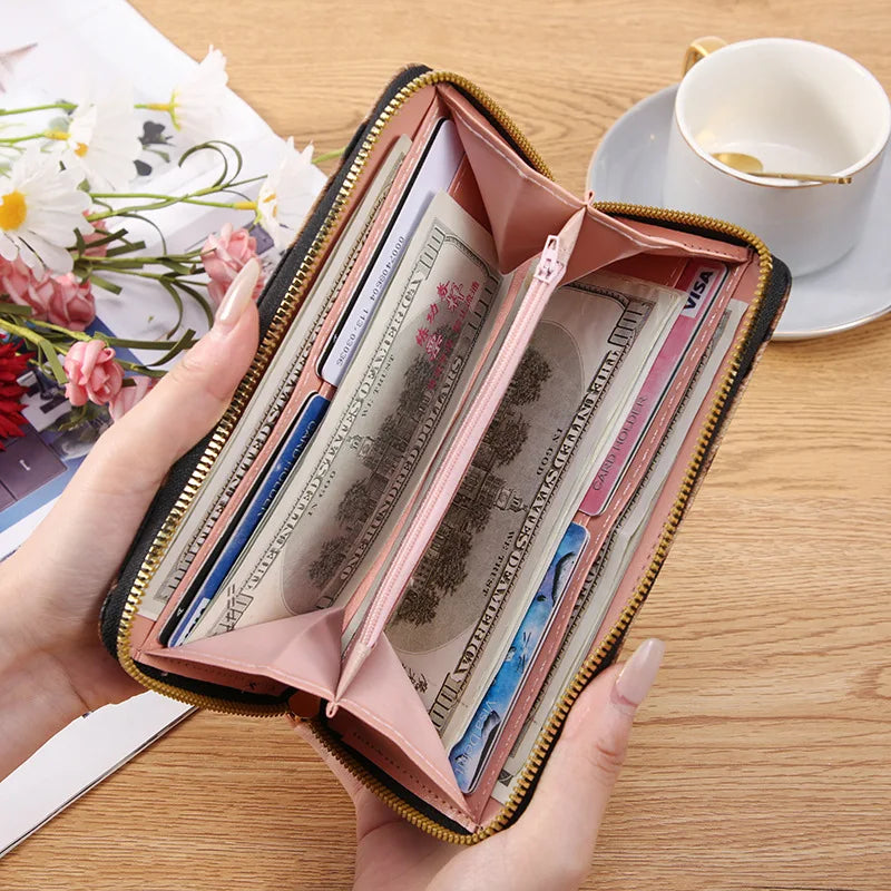 A hand holds an open pink wallet with a gold zipper, displaying various banknotes and cards on a wooden surface.