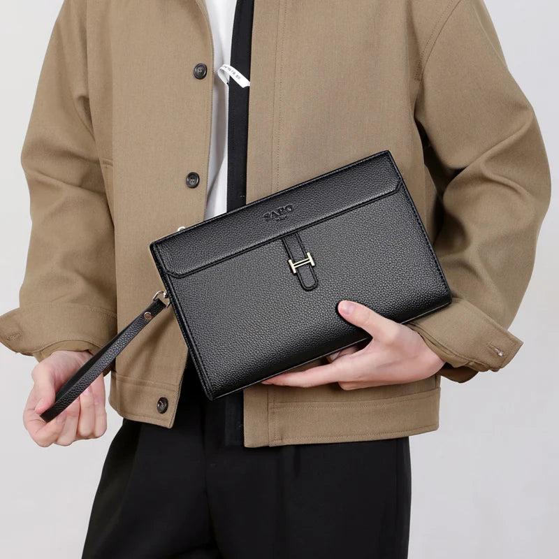 Eine Frau hält eine schwarze Kunstleder-Clutch vor ihrem Oberkörper, trägt eine beige Jacke.