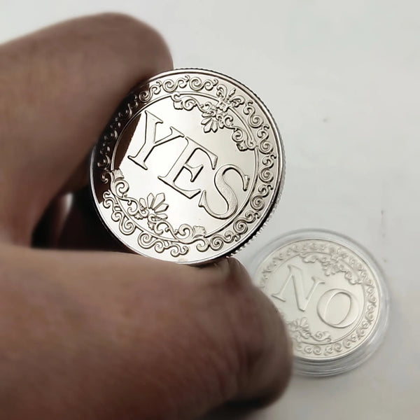 A hand holds a silver commemorative coin with the word YES stamped on one side and NO on the other.