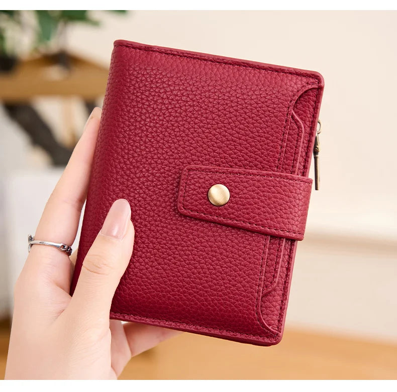 A hand holds a deep red textured leather bifold wallet with a flap closure.
