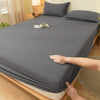 A hand is folding a gray soft brushed fitted sheet on a wooden bed.