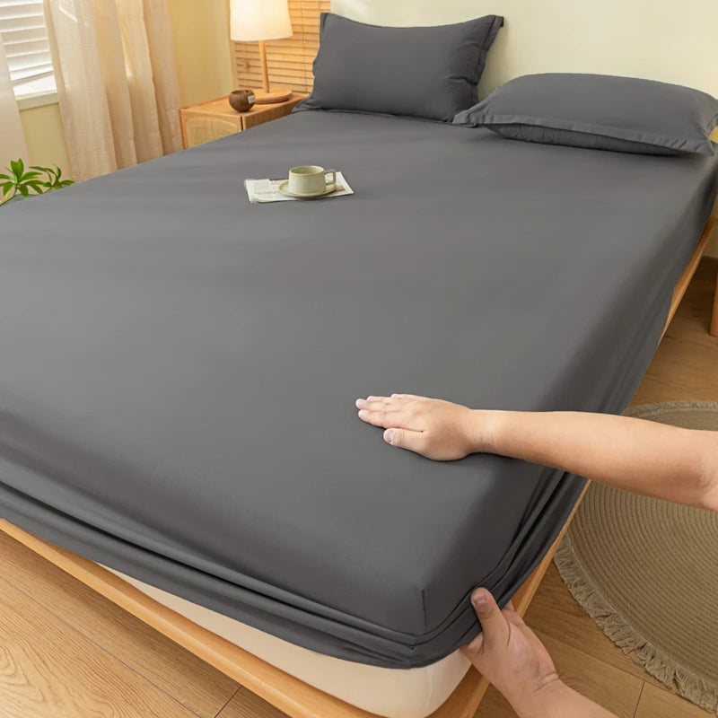 A hand is folding a gray soft brushed fitted sheet on a wooden bed.