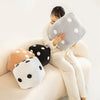A woman is holding a large, gray and white polka-dotted plush pillow on her lap.