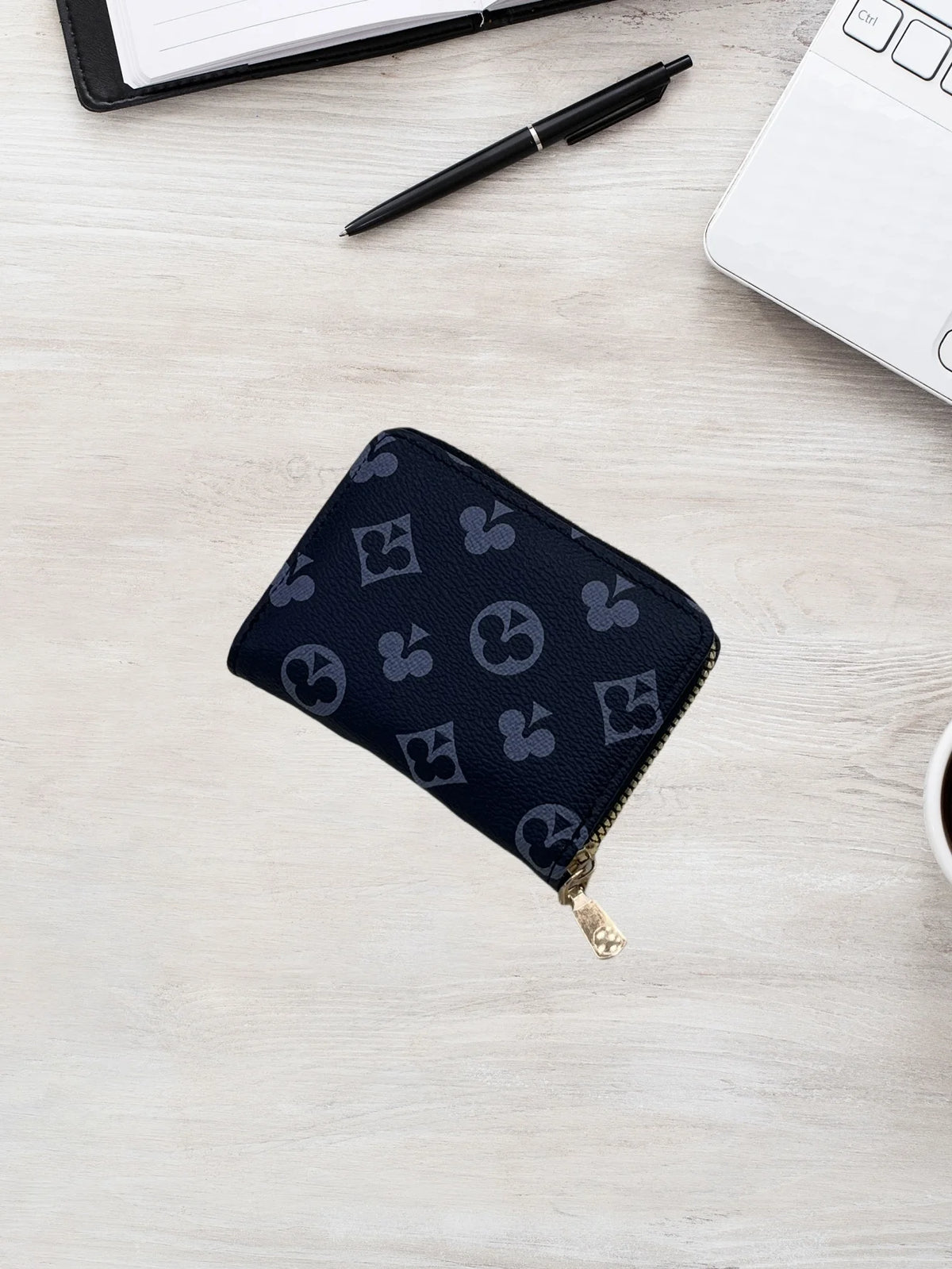 A dark navy zippered card holder wallet with a repeating geometric pattern rests on a light wooden surface next to a pen and 