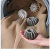 A hand holds a grey reusable laundry ball for pet hair and lint removal against a beige fabric background.