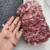 A hand holding a skein of pink and mauve variegated cotton blend yarn for knitting and crochet.