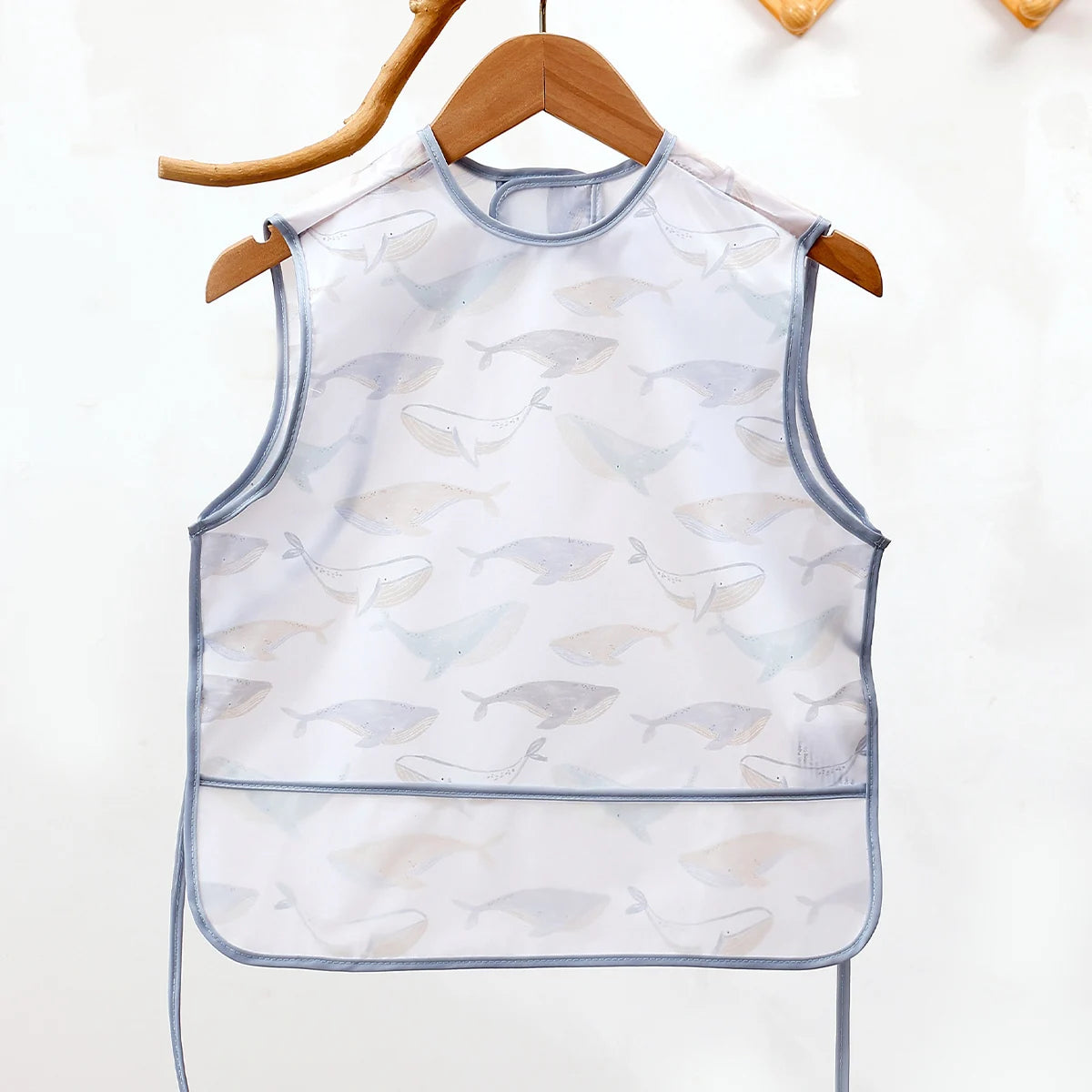 White waterproof full-body baby feeding bib with a sleeveless design featuring light blue and beige fish patterns