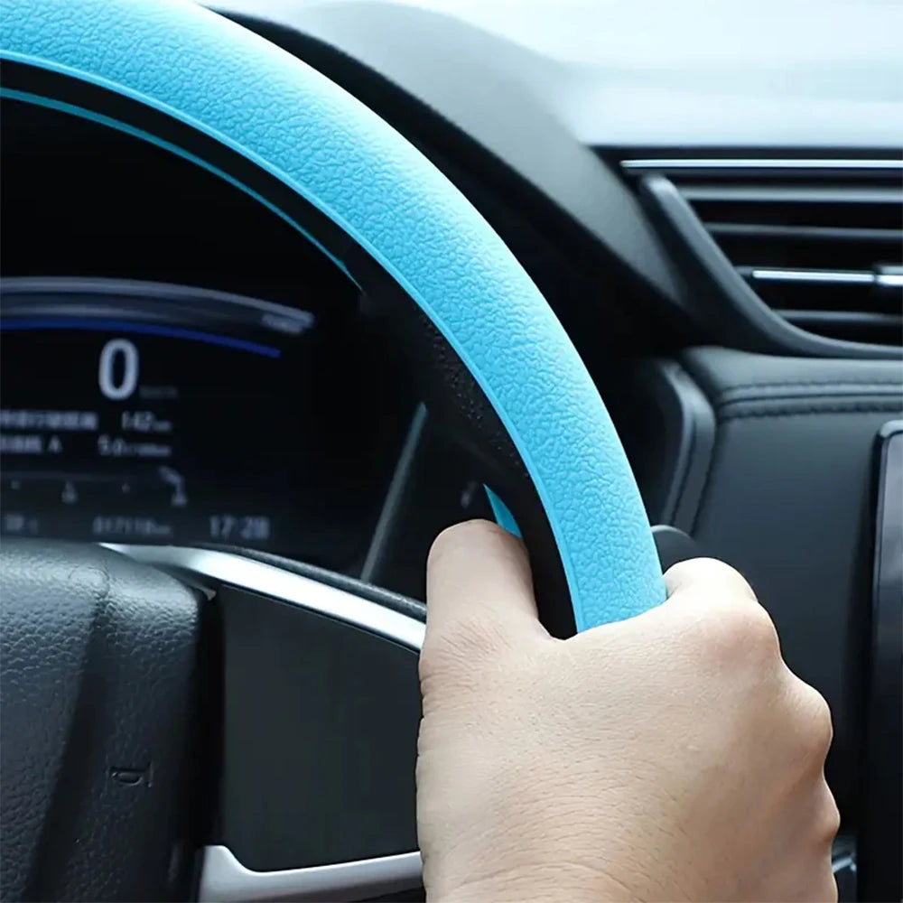 A hand grips a light blue silicone steering wheel cover on a black car steering wheel.