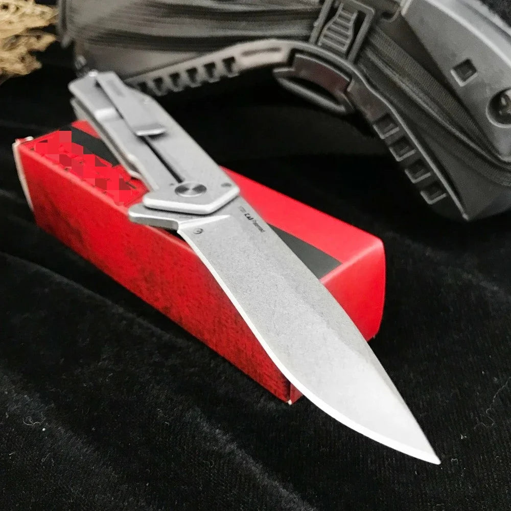 A silver folding pocket knife is displayed on a red box next to a black fabric, with part of a dark tactical firearm visible 