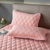 Pink quilted pillow protector with a pink pillow and a green glass bottle on a gray background.