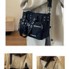 A black nylon shoulder bag with chain accents is shown being held by a person in a light beige coat.