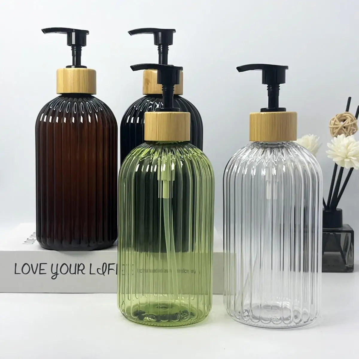 A set of three refillable soap dispensers in dark brown, green, and clear glass with wooden caps.