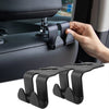 A hand is shown using black universal car headrest hooks to hang a handbag or coat.