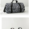 A black and white leopard print travel tote bag with shoulder straps resting on a white surface.