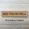 A rectangular tan woven patch with black text that reads SEE YOU IN HELL on a light wooden surface.