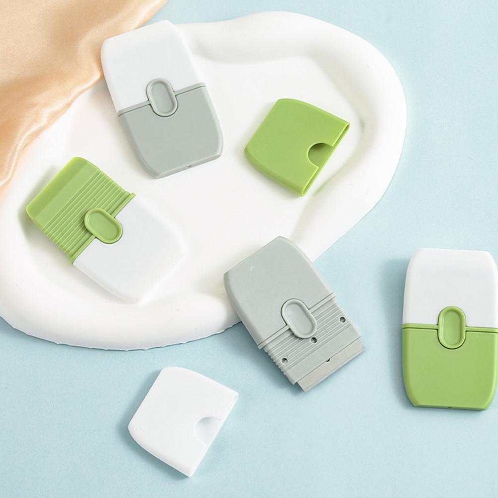 A collection of double-ended cleaning scrapers in white and light green plastic resting on a white tray.