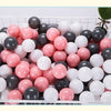 A white plastic basket filled with a pack of colorful pink and black ball pit balls for toddlers.