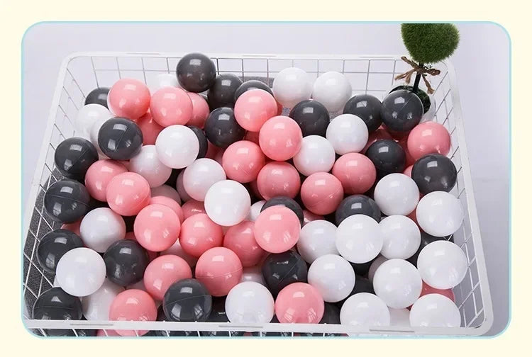 A white plastic basket filled with a pack of colorful pink and black ball pit balls for toddlers.