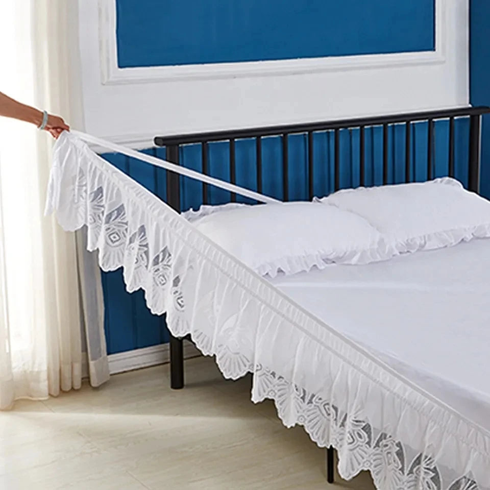 White jacquard lace bed skirt with elastic band draped over a dark metal bed frame.
