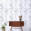A wooden dresser is displayed against a white wall covered in a gray and green leaf peel-and-stick wallpaper.