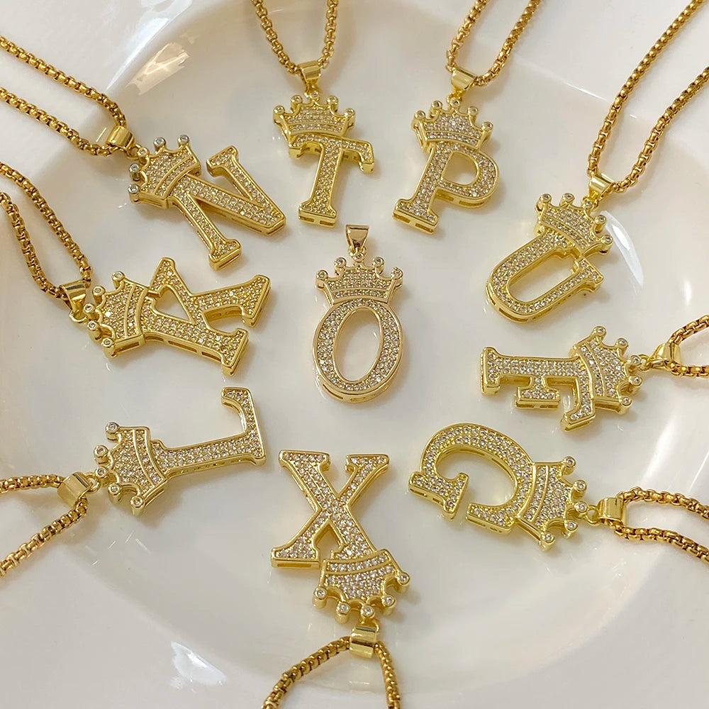 A collection of gold-toned letter pendants and crown charms displayed on a white surface.