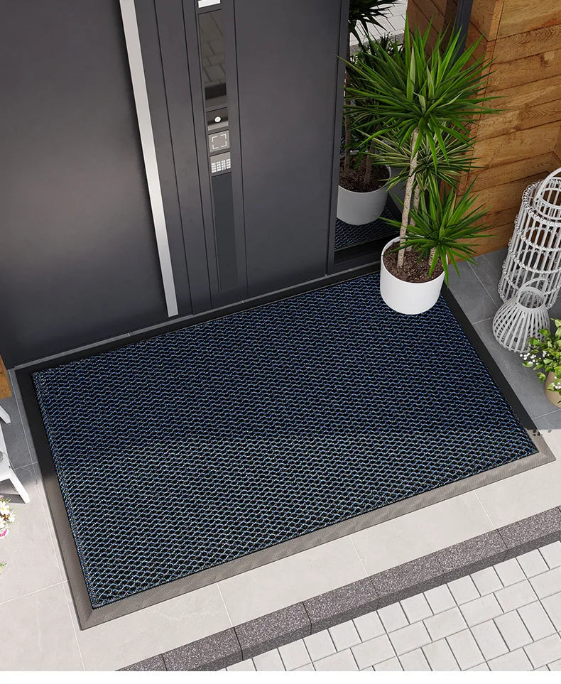 A dark blue hexagonal non-slip doormat placed on a gray tiled floor outside a modern door.