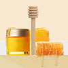 A glass jar of golden honey next to a wooden dipper stick and a piece of honeycomb.