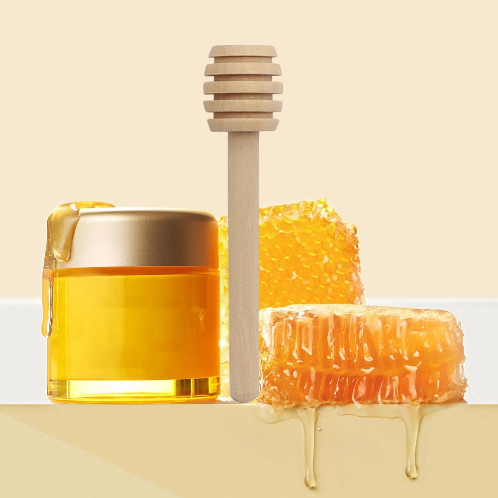 A glass jar of golden honey next to a wooden dipper stick and a piece of honeycomb.