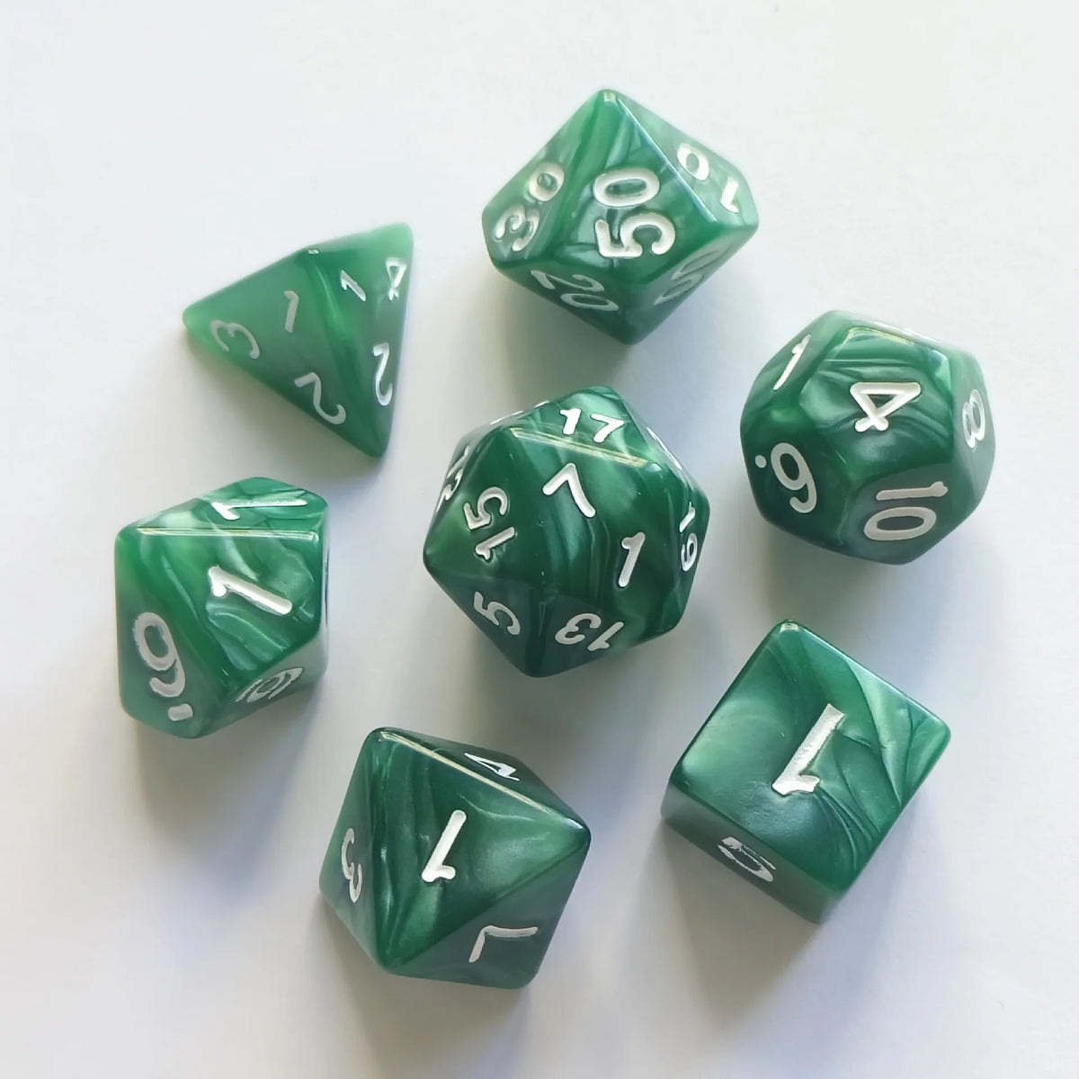 A set of seven green pearl pattern polyhedral dice arranged on a white surface.