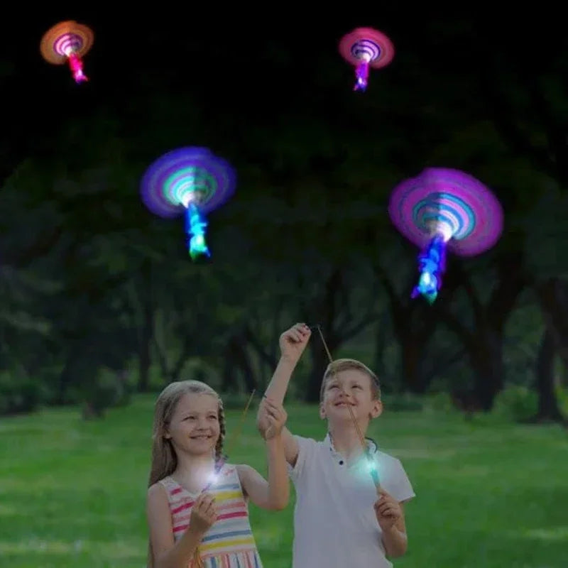 Two children are playing with an LED glowing flying arrow toy outdoors in a grassy park.