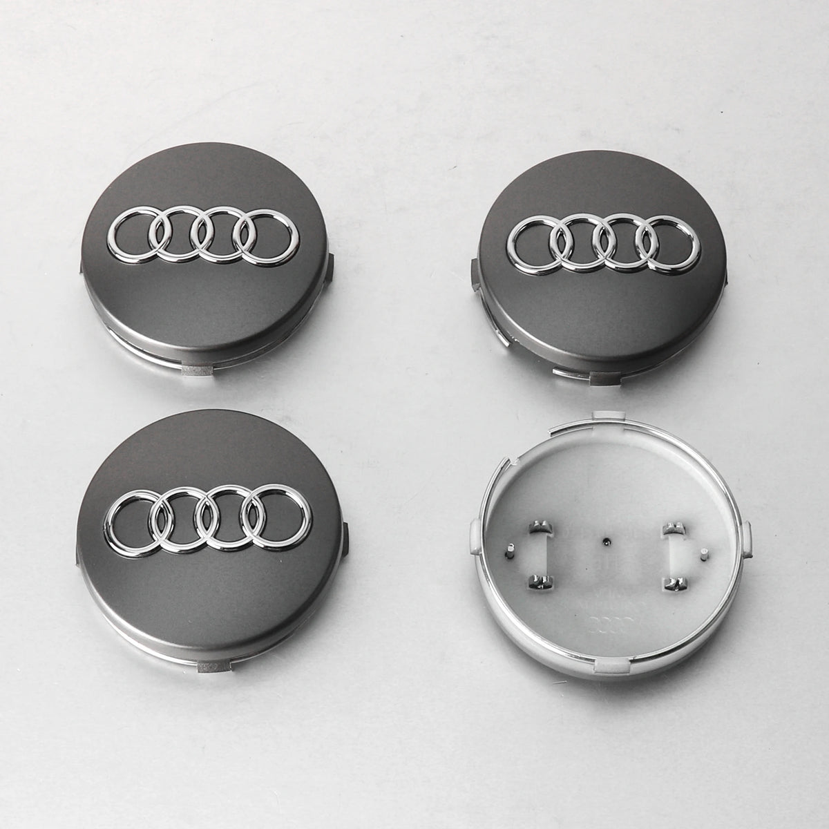 Four views of Audi center hub caps with decorative wheel covers, showing the logo and mounting mechanism.