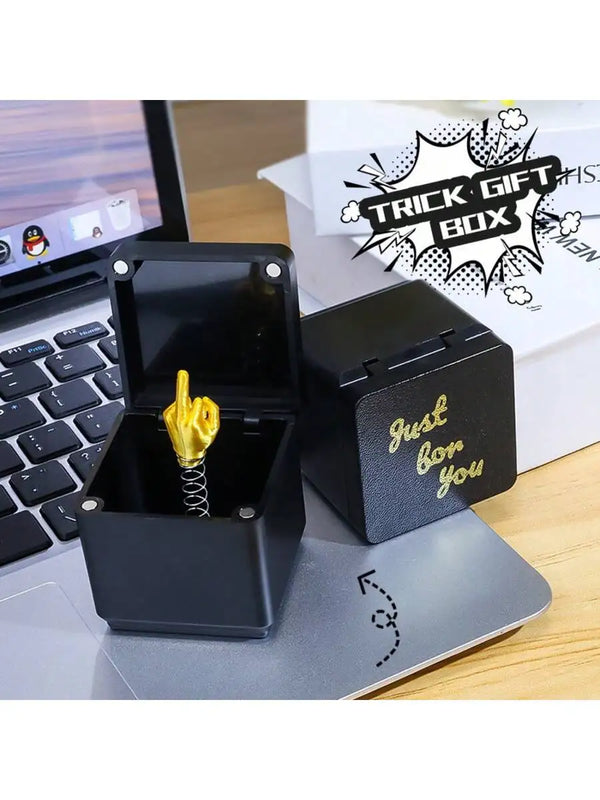 Une boîte cadeau noire avec une statue de main dorée sur un ordinateur portable argenté.