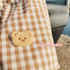 A cute bear patch is placed on a tan and white checkered fabric.