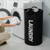 A black laundry basket with padded handles is placed next to a white washing machine.