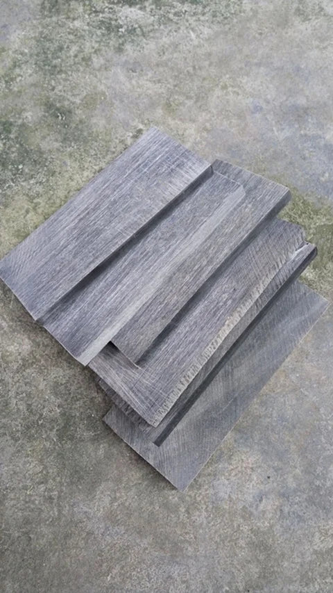 Two stacked black buffalo horn knife handle scales showing wood grain texture on a gray stone surface.
