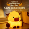 A cute silicone Highland calf night light glowing yellow on a wooden surface.
