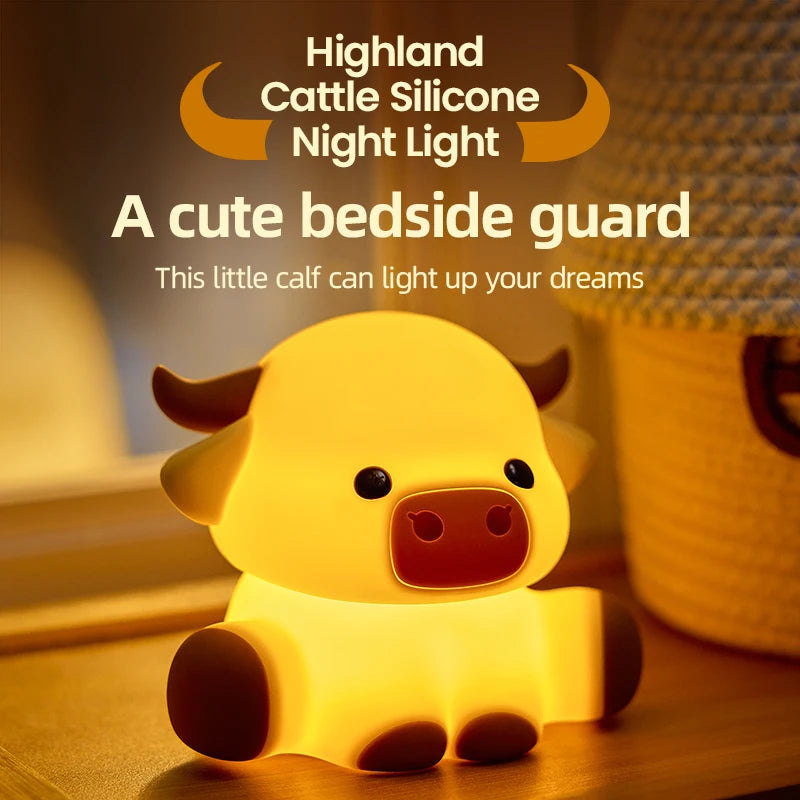 A cute silicone Highland calf night light glowing yellow on a wooden surface.