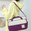 A person holds a purple and white multifunctional crossbody diaper bag set against a white background.
