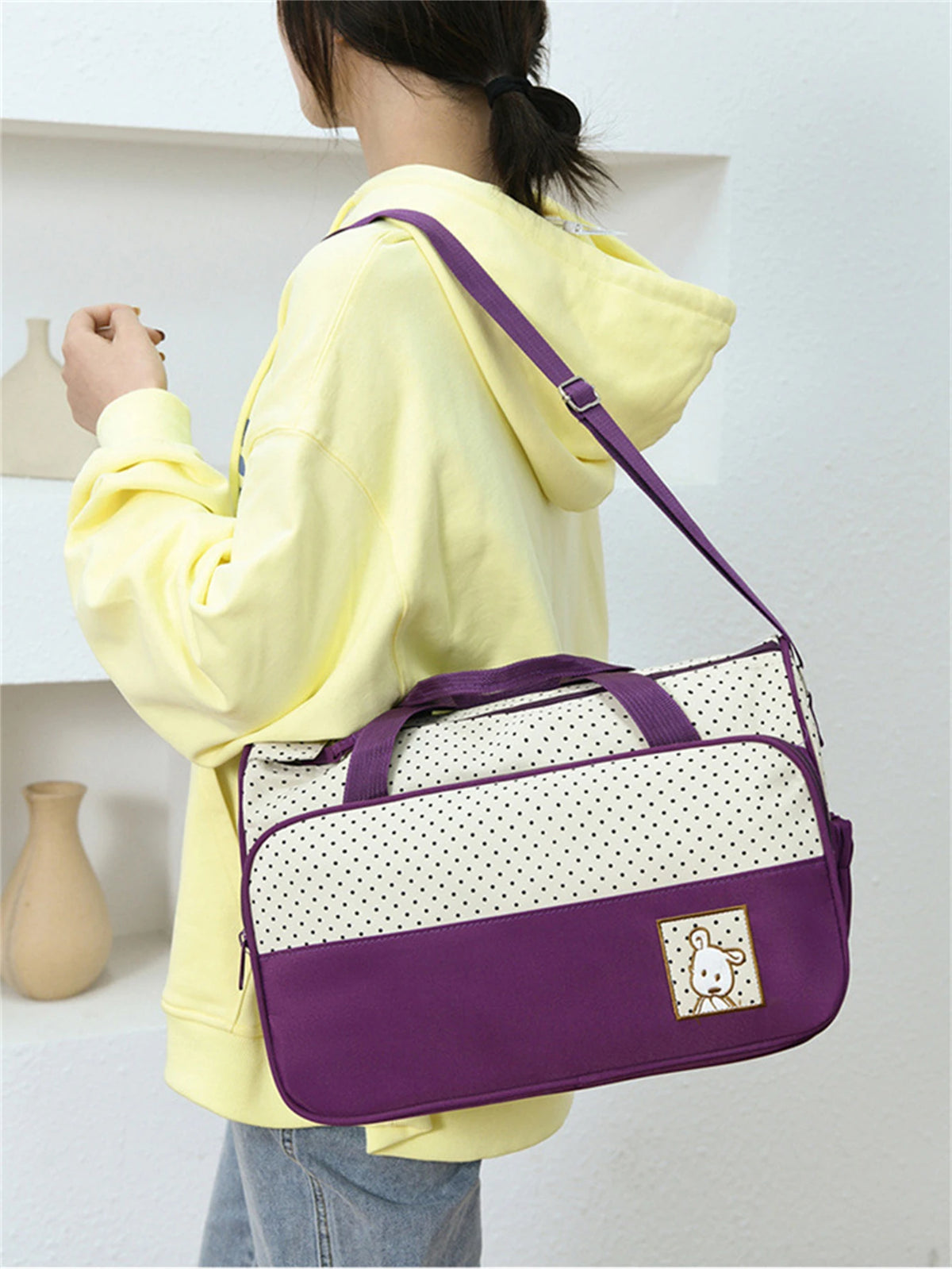 A person holds a purple and white multifunctional crossbody diaper bag set against a white background.